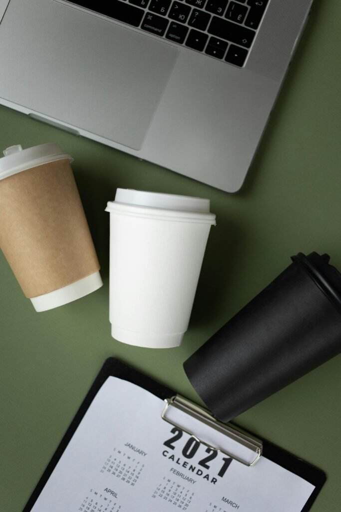 Coffee cups and 2021 calendar on a green background, next to a laptop. Perfect for office themes.